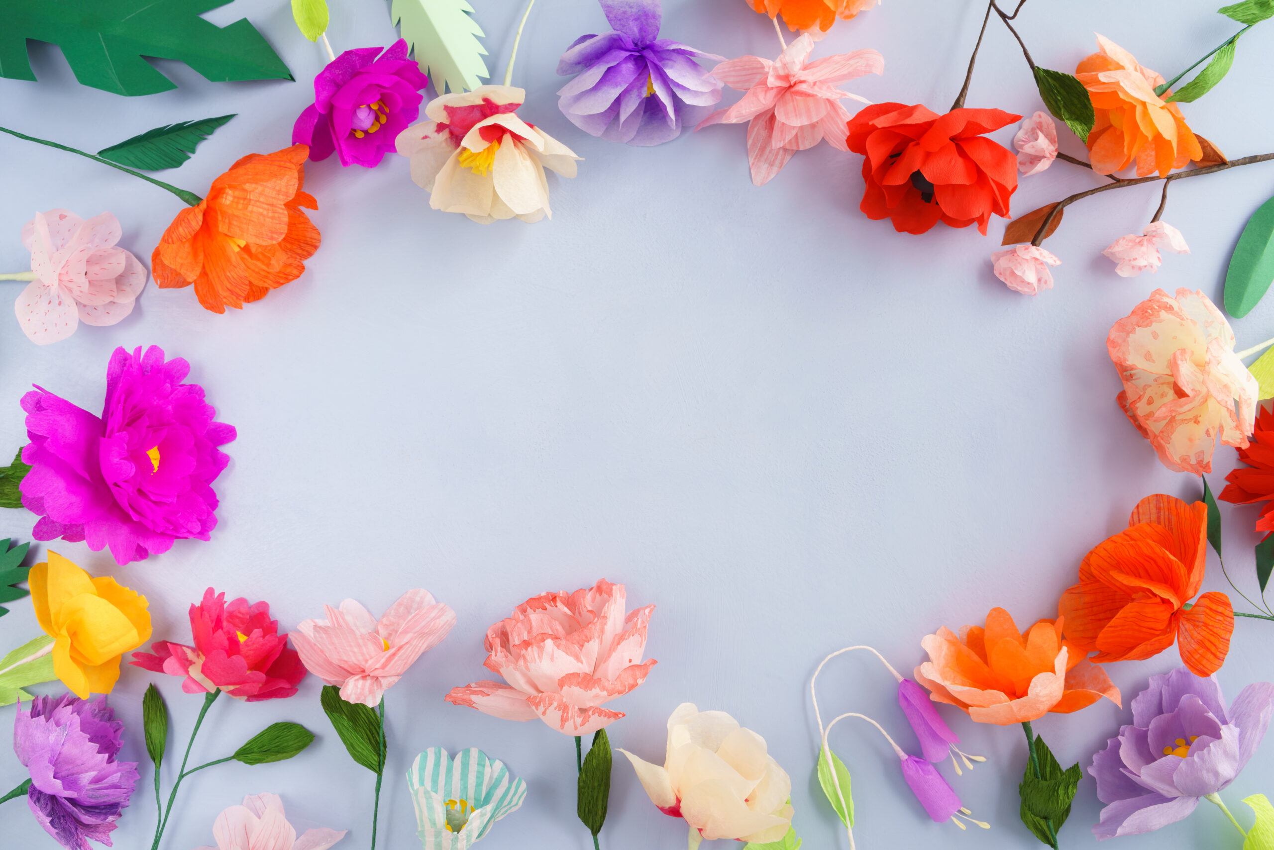 Colourful handmade paper flowers on light blue background with copyspace in the center